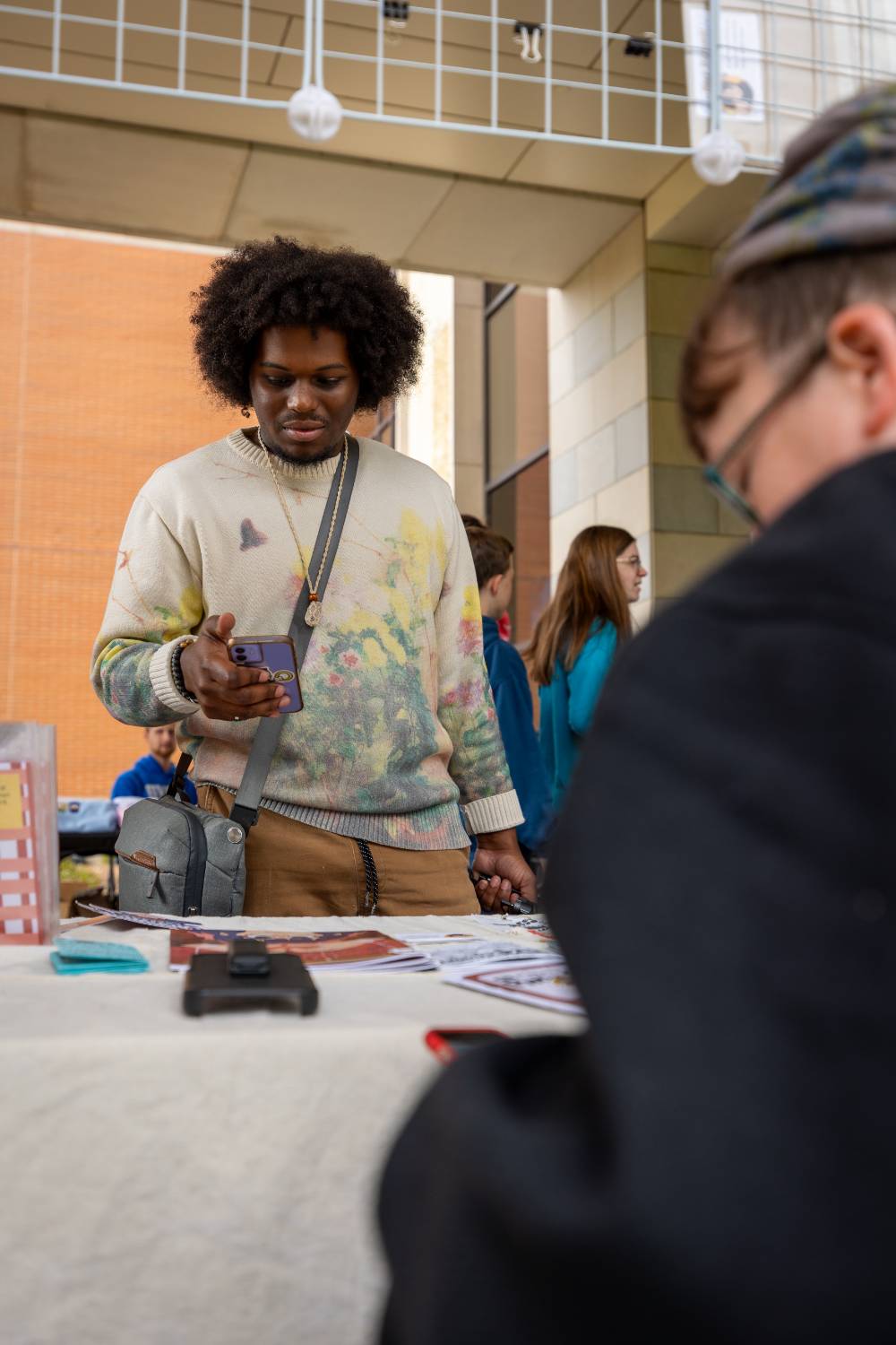 Student holds cell phone while looking at display during Student Small Business Market.